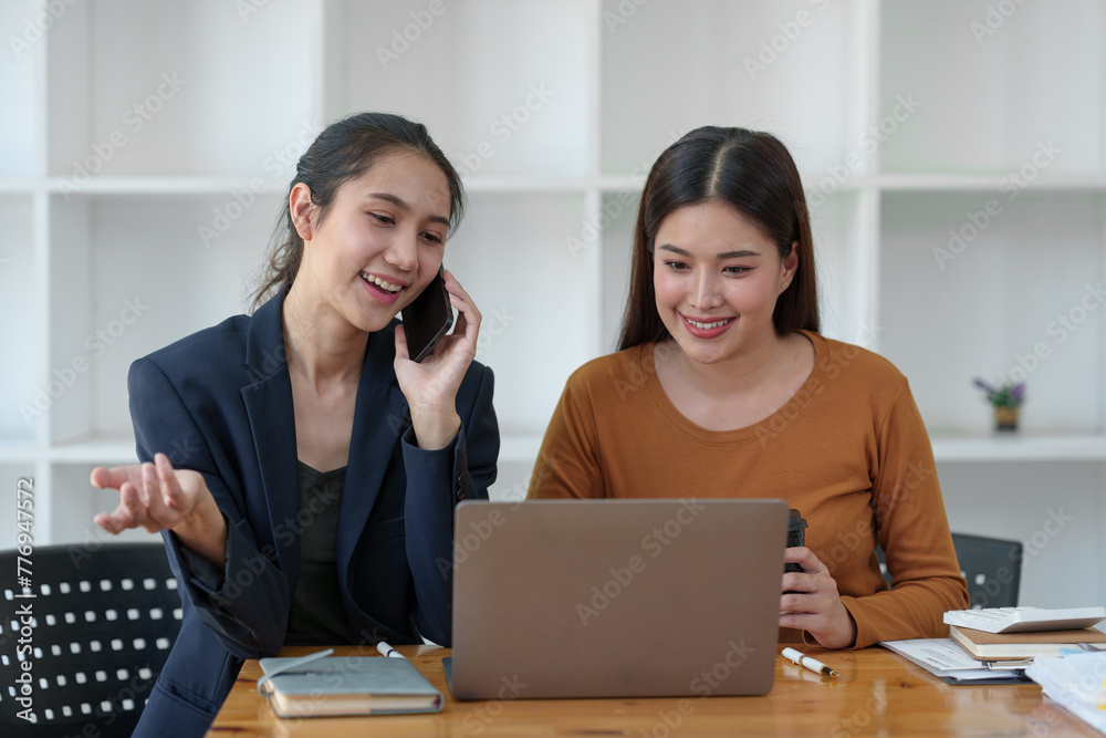 Two beautiful business women smiling happily and expressing their opinions, talking, discussing Investment approved with acceptance documents and laptop computer in office. Two beautiful business women smiling happily and expressing their opinions, talking, discussing Investment approved with acceptance documents and laptop computer in office.