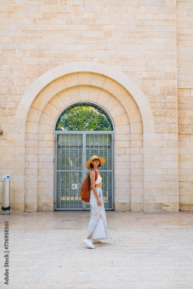 Back view of a hipster girl traveler in a hat and backpack traveling alone through the sights of Israel.
