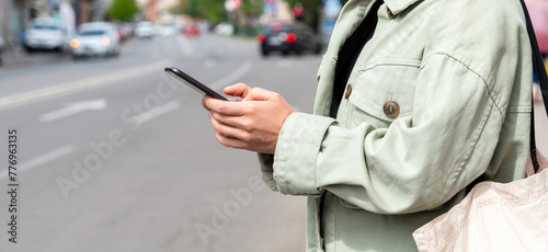 Bild auf Leinwand Female person uses mobile phone to search for car rental, car-sharing or taxi while standing by the roadside in city