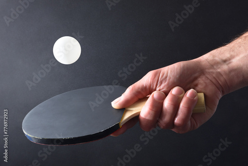 Ping-pong player hitting ball with paddle on black isolated background