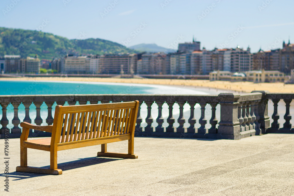 Naklejka premium Wooden bench at promenade Beach of La Concha in San Sebastian, Basque country, Spain