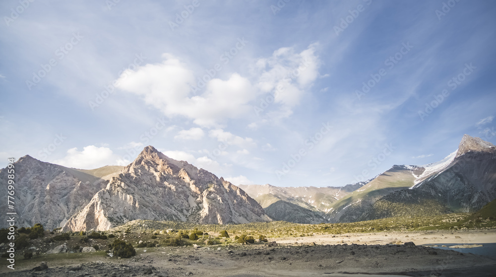 Mountain panoramic landscape of the Fan Mountains with rocks, glaciers and vegetation in sunny weather with blue sky, mountain panorama in Tajikistan in the early evening
