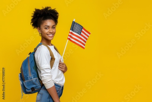 Beautiful confident black student girl standing on yellow copy space background. Happy proud African American college or university student with backpack holding US flag and smiling