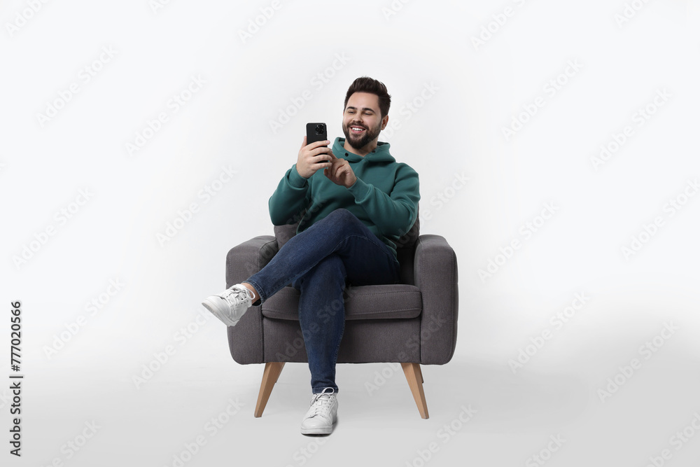 Happy young man using smartphone in armchair on white background Happy young man using smartphone in armchair on white background