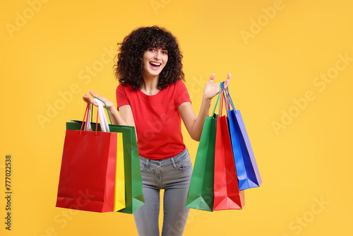 Happy young woman with shopping bags on yellow background