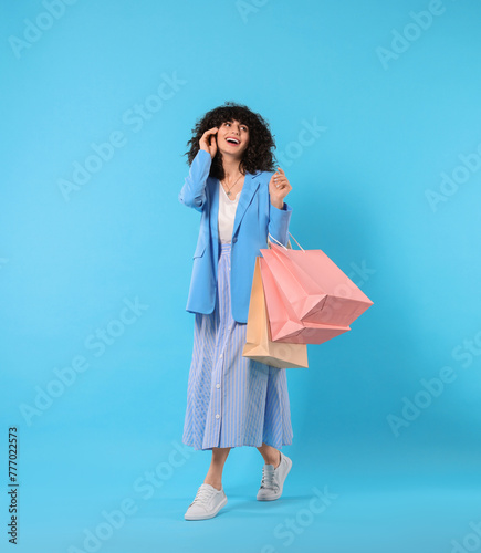 Happy young woman with shopping bags on light blue background. Space for text
