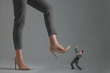 Big woman stepping onto small man on grey background
