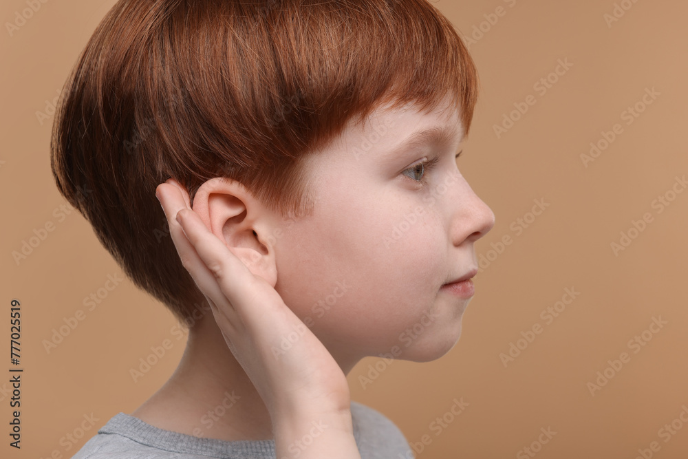 Little boy with hearing problem on pale brown background, closeup Little boy with hearing problem on pale brown background, closeup