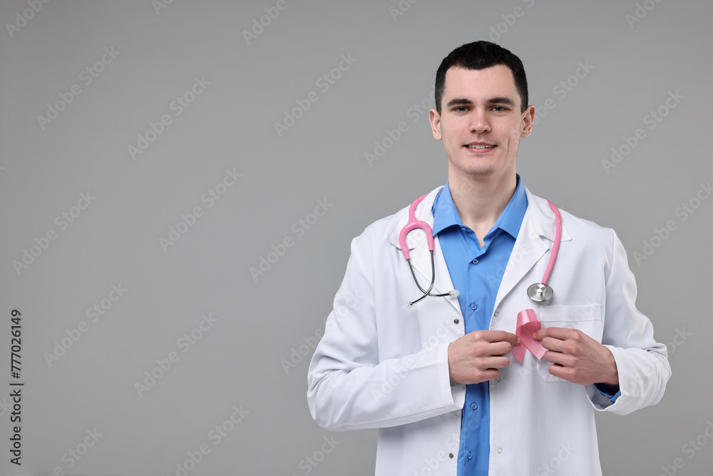 Portrait of smiling mammologist with pink ribbon and stethoscope on grey background. Space for text Portrait of smiling mammologist with pink ribbon and stethoscope on grey background. Space for text