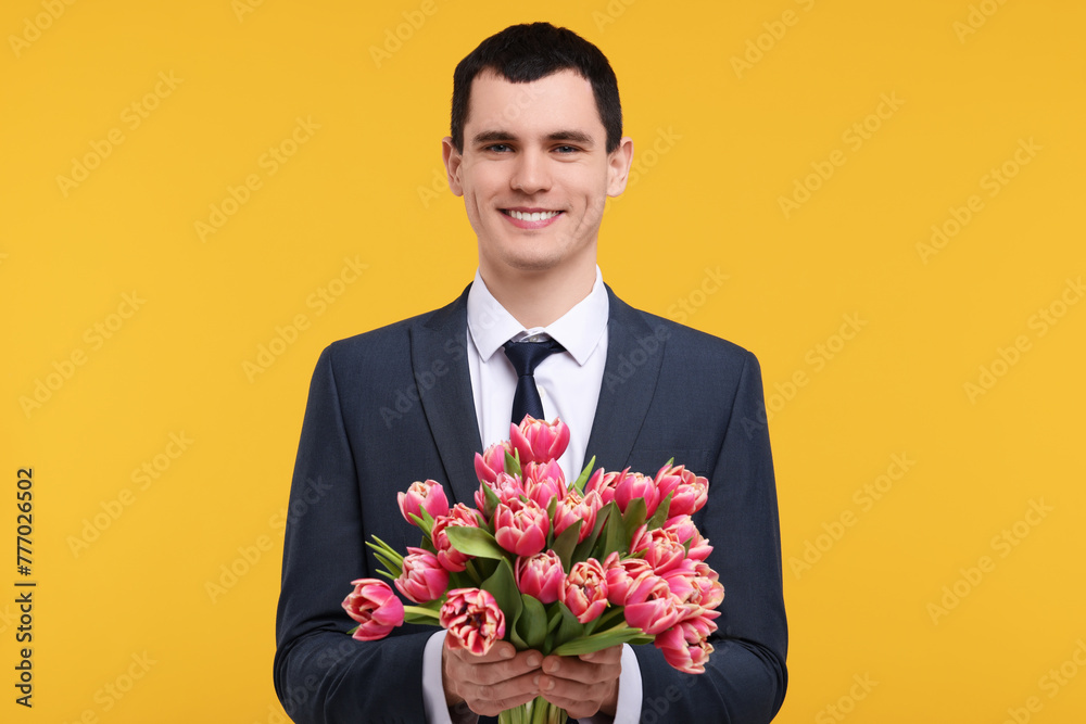 Happy young man with beautiful bouquet on orange background Happy young man with beautiful bouquet on orange background