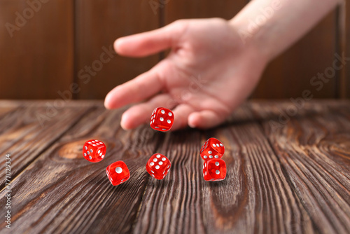 Woman throwing red dice on wooden table, closeup