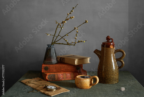 Still life with a cup of aromatic coffee, flowering willow branches, an old ceramic teapot, books and a pocket watch with a chain.