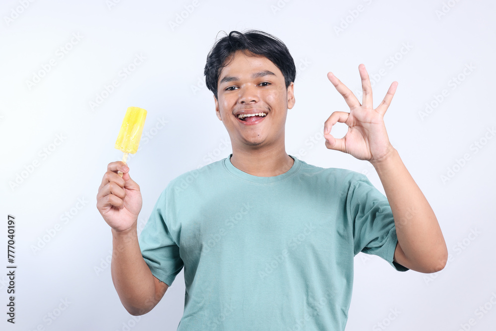 Happy young Asian man holding ice cream stick and showing ok sign with fingers Happy young Asian man holding ice cream stick and showing ok sign with fingers