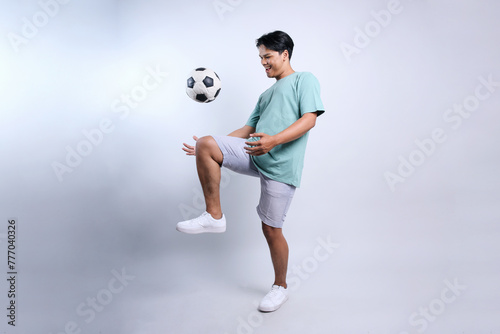 Fototapeta Naklejka Na Ścianę i Meble -  Full length view of young Asian stylish man playing soccer with happy expression
