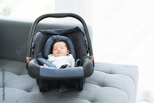 Portrait of adorable less than one month old newborn baby girl sleeping in the modern car seat with fastening safety belt at home. Selective focus on little Asian Australian child