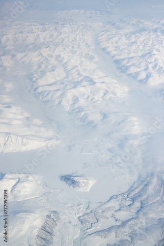 Winter aerial photograph of Lake Verkhniy Ilirnei. Chukotka, Russia. Top view of an ice-covered lake. There is an island in the center of the lake. There are snow-capped mountains around. Arctic.