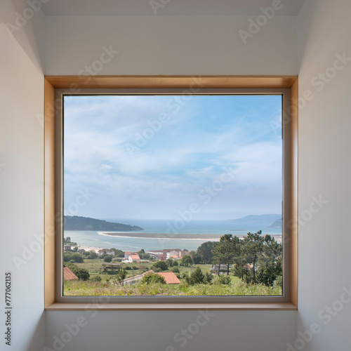 Large square window framed between white walls. Views of a coastal landscape