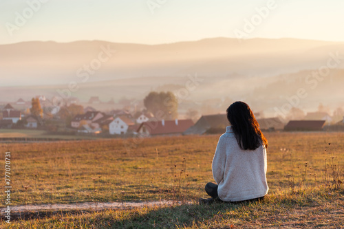 woman sitting in the field at sunset in front of a city