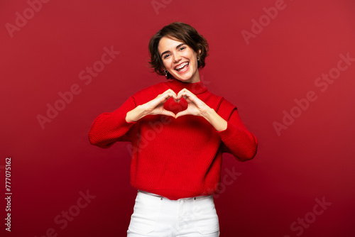 Portrait photo of joyful, attractive woman making a heart gesture with her hands photo