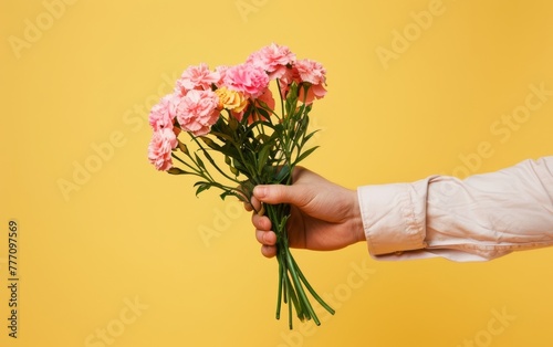 An arm extends to offer a bunch of soft pink carnations  set against a sunny yellow background  epitomizing springtime cheer.