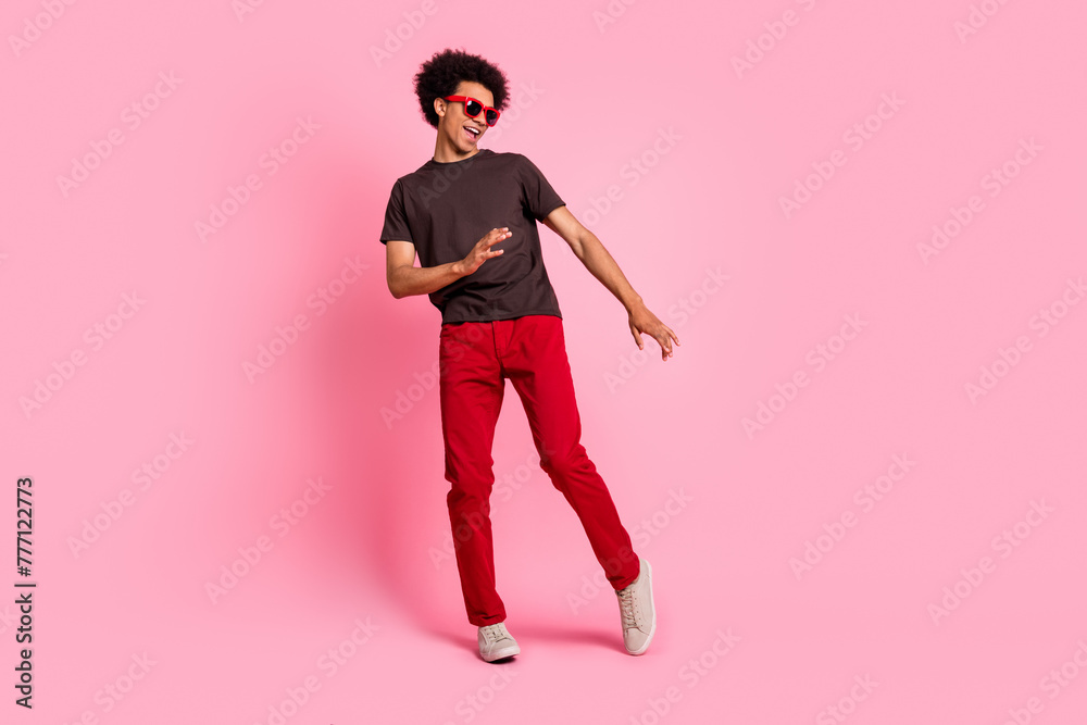 Full body length photo of millennial curly hair man dance in eyewear brown t shirt and red pants isolated on pink color background