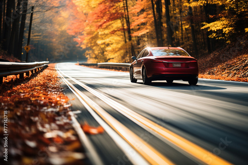 Car driving on a tarmac road surrounded by autumn foliage at sunset.  