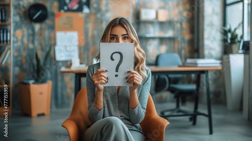 Woman in a modern office covering her face with a question mark sign. Concepts: self-discovery, self-presentation, psychology, privacy, communication, mental health