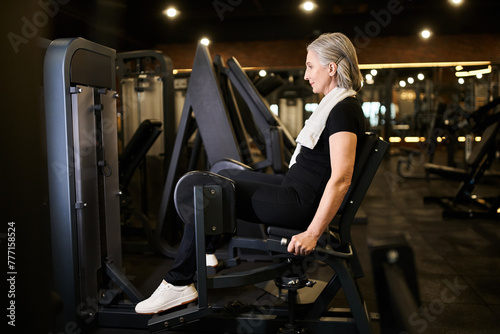 good looking athletic senior woman in sportswear training actively on calf machine while in gym