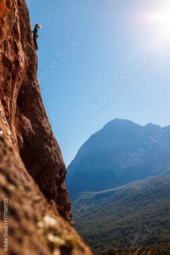 girl climber climbs a rock against a background of forest and mountains. rock climber resting on a difficult route.