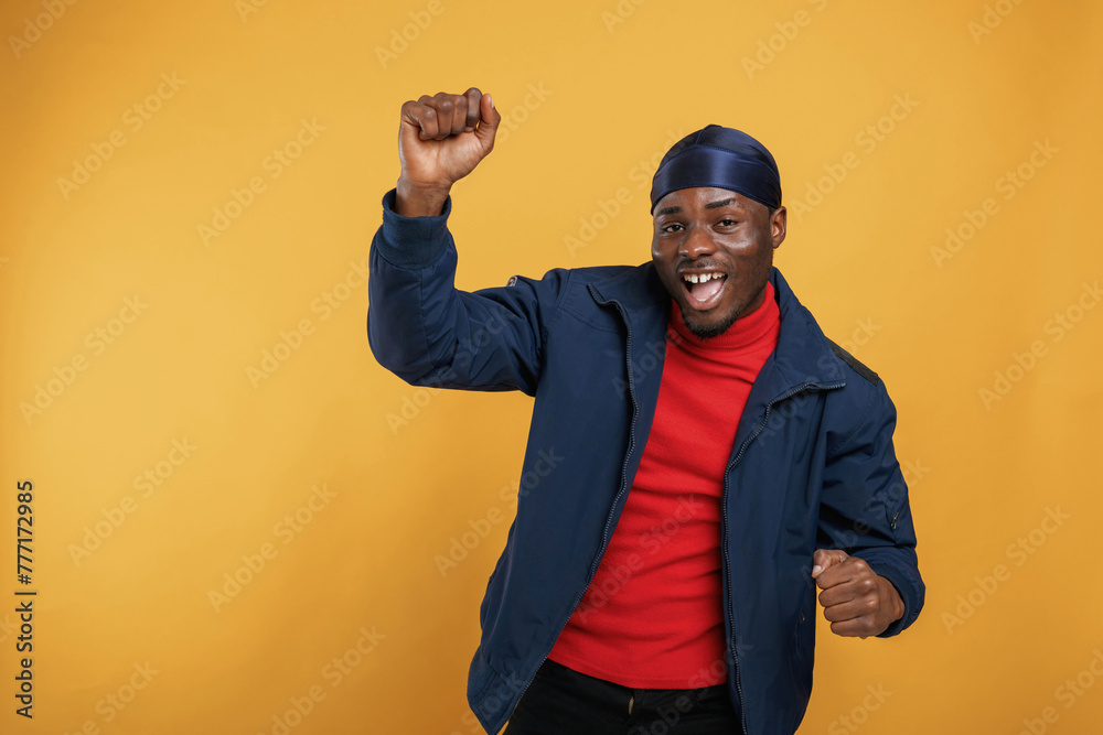 Naklejka premium Having fun, celebrating success, hands up. Handsome black man is in the studio against yellow background