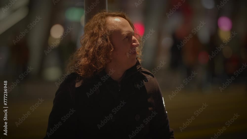 A man with long curly hair is seen sitting on the sidewalk at night, contemplating life. The darkness of the setting adds a sense of mystery and introspection to the scene A man with long curly hair is seen sitting on the sidewalk at night, contemplating life. The darkness of the setting adds a sense of mystery and introspection to the scene