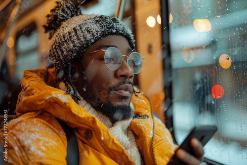 A person covered in snowflakes is focused on their phone while snow falls outside the bus window they're seated by