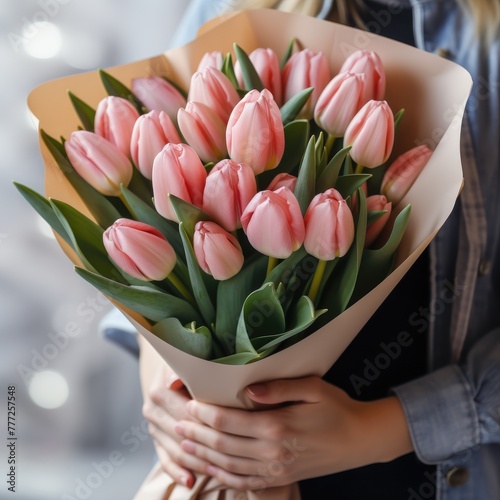 A large bouquet of tulips wrapped into white paper, holded by a young woman