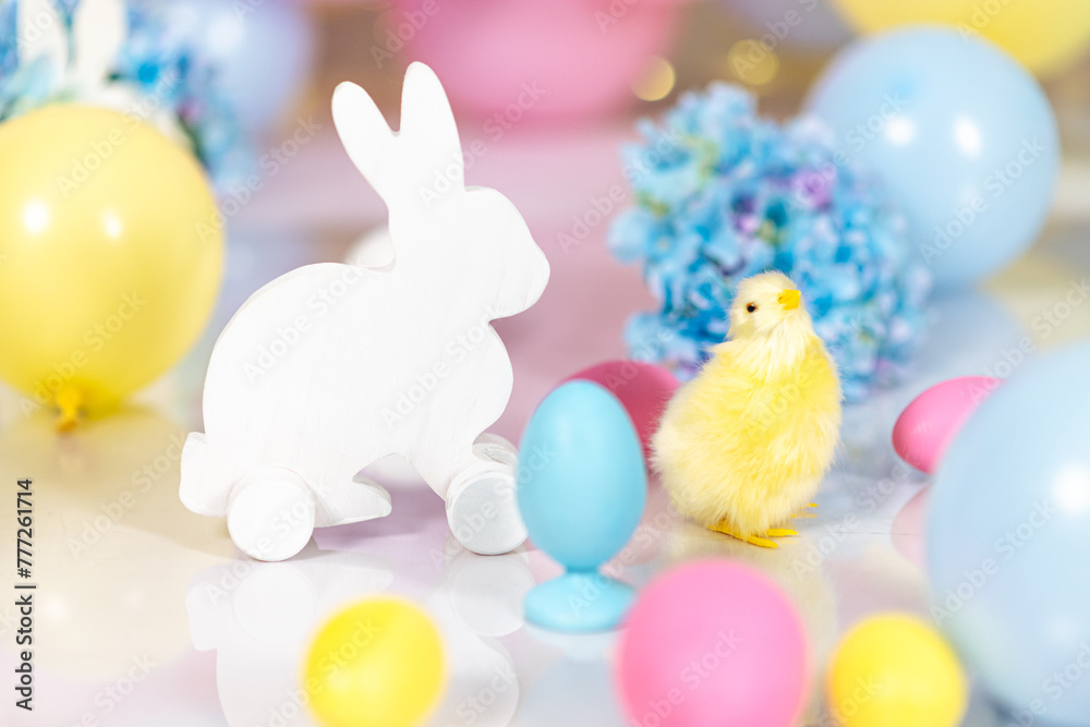 Fototapeta premium A figurine of a white Easter bunny against a background of Easter eggs, multi-colored pastel balls and blue hydrangeas