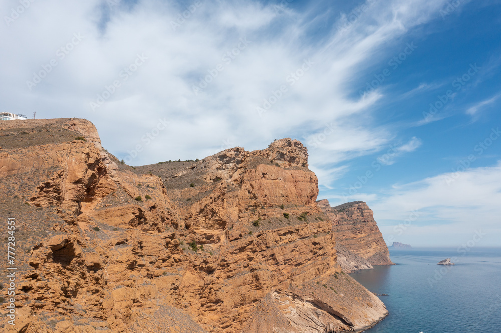 Aerial drone photo of the rocky cliffs located in the town of Benidorm in Spain and a sunny summer day with blue sky and white clouds.