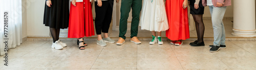 A group of people are standing in a room, with some wearing red and others wearing white. Scene is casual and friendly, as the people are posing for a photo together.