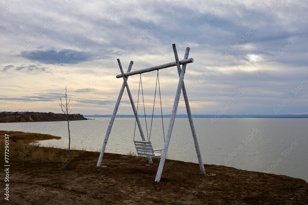 Swing on a cliff. View of the lake at winter sunset Swing on a cliff. View of the lake at winter sunset