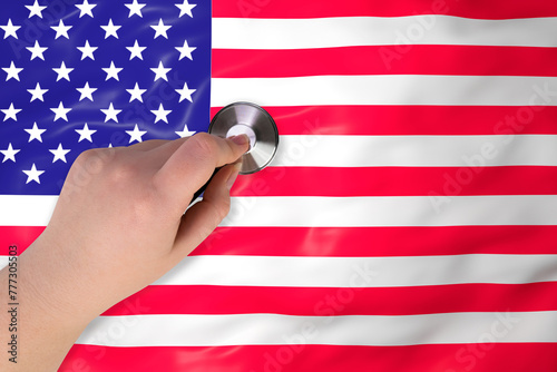 The head of a medical stethoscope in a hand (close-up) against the background of the US flag. US healthcare system concept