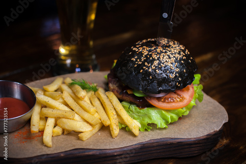 A black burger with a knife on it sits on a wooden board with a side of french fries