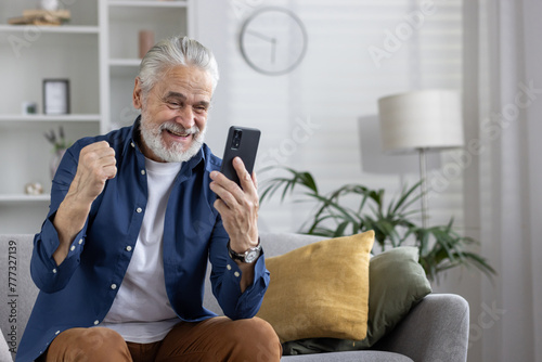 Senior man celebrating good news on phone at home