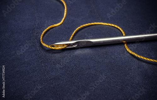 A needle with a thread is on a blue surface.