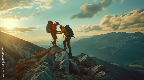 Two people are seen standing on top of a rocky mountain peak.  They appear to be supporting each other on the steep terrain. Majestic mountain range under a light blue sky with a few white clouds photo