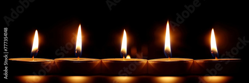 A row of burning white candle on black background