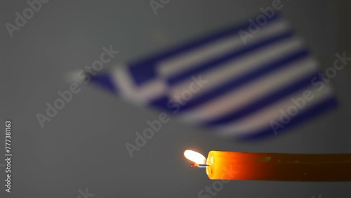 Burning wax candle against the background of a blurred Greek flag. Vertical. photo