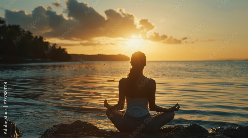 Young woman meditating in lotus position at sunset on the beach