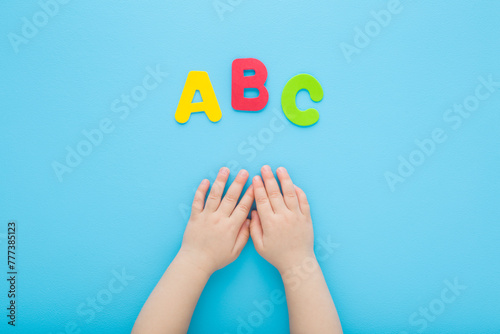 Baby boy hands and colorful abc letters on light blue table background. Pastel color. Time to learning. Closeup. Point of view shot. Top down view.