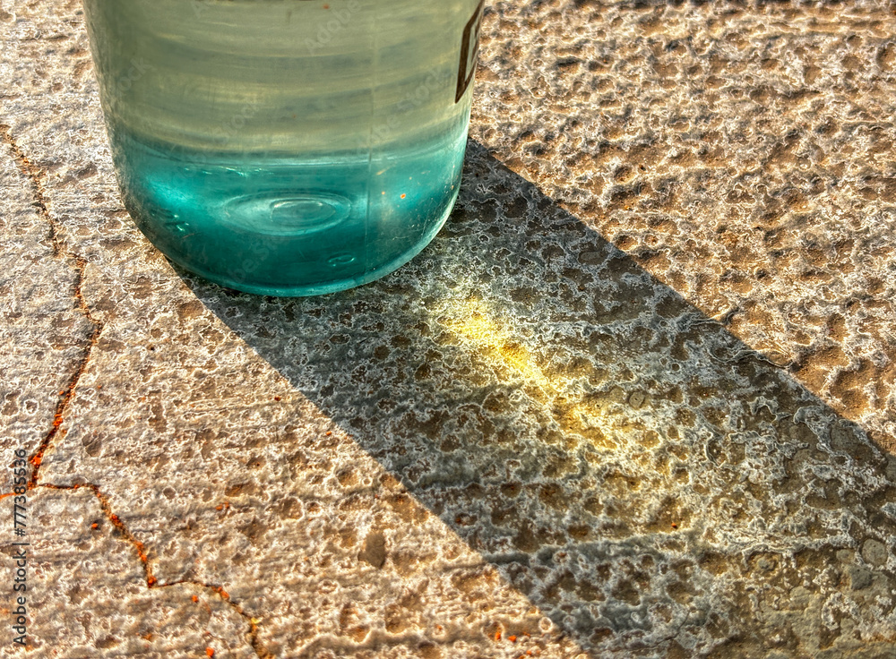 An abstract photo with glass bottle place on rough textured surface, sunlight hitting the bottle from the side
