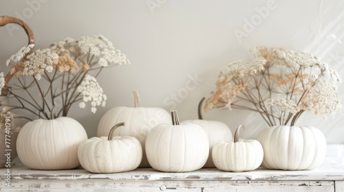 Autumnal decoration with white pumpkins and dried flowers on a rustic white wooden surface.