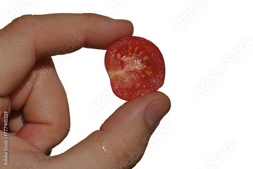 Half sliced cherry tomato (Solanum Lycopersicum var Cerasiforme) held between thumb and index finger of adult person, white background. 