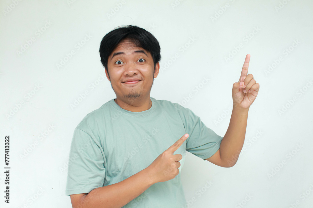 Young asian man in green t-shirt with happy expression. While pointing up. Isolated on gray background. Young asian man in green t-shirt with happy expression. While pointing up. Isolated on gray background.